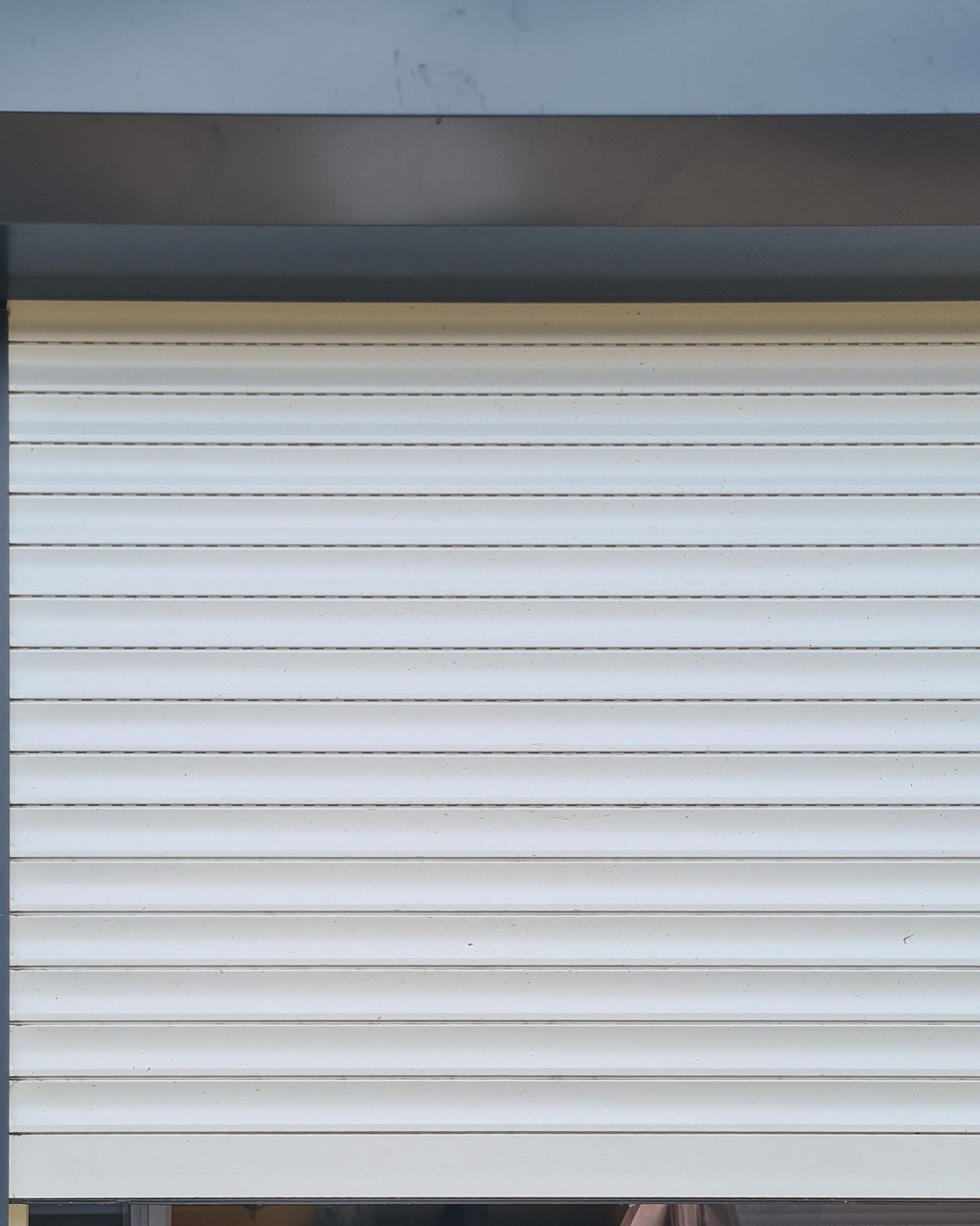 Wit rolluik, neergelaten voor een raam in een antracietkleurig kozijn